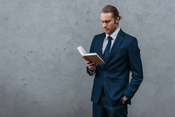 Молодий серйозний бізнесмен читає книгу перед бетонною стіною — стокове фото