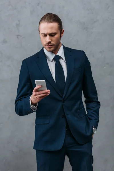 Handsome confident businessman using smartphone in front of concrete wall — Stock Photo