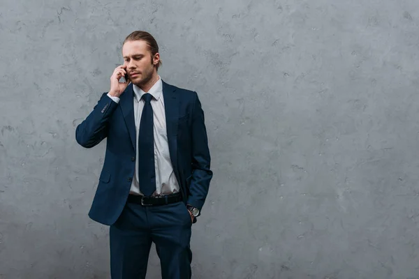 Serious handsome businessman talking by phone in front of concrete wall — Stock Photo