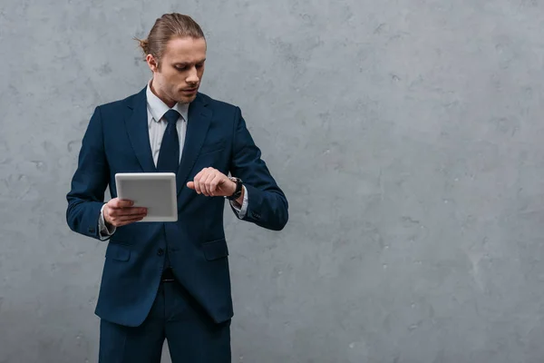 Jeune homme d'affaires beau avec tablette regardant la montre devant le mur de béton — Photo de stock