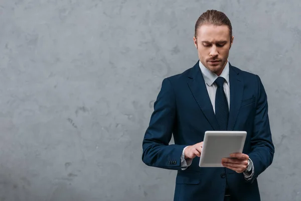 Joven empresario serio utilizando tableta delante de la pared de hormigón - foto de stock