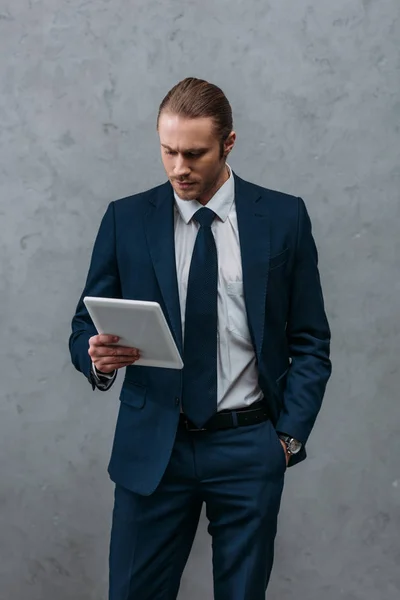 Young handsome businessman using tablet in front of concrete wall — Stock Photo