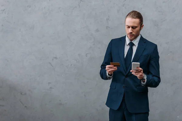 Junger gutaussehender Geschäftsmann mit Kreditkarte und Smartphone beim E-Shopping — Stockfoto