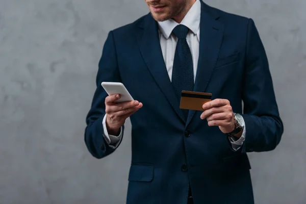 Recortado tiro de hombre de negocios con tarjeta de crédito y teléfono inteligente haciendo e-shopping - foto de stock
