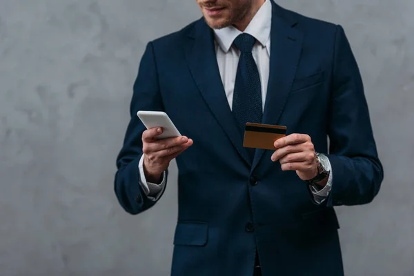 Tiro recortado de empresário com cartão de crédito e smartphone fazendo e-shopping — Fotografia de Stock