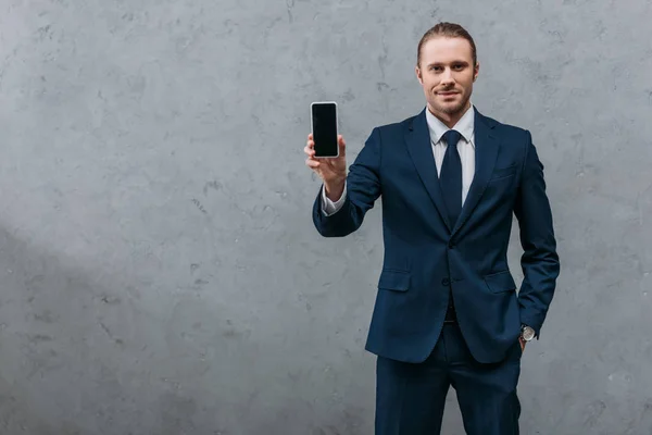 Young handsome businessman showing smartphone at camera — Stock Photo