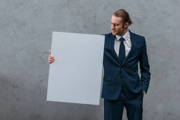 Jovem homem de negócios elegante segurando placa em branco na frente da parede de concreto — Fotografia de Stock