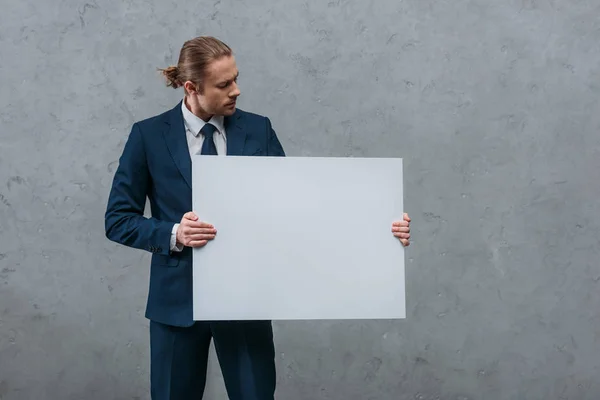 Young handsome businessman holding blank board in front of concrete wall — Stock Photo