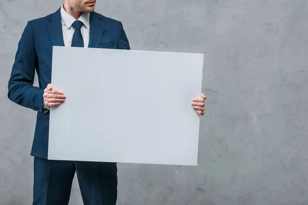 Cropped shot of businessman holding blank board in front of concrete wall — Stock Photo