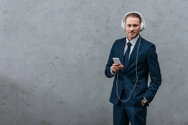 Jeune homme d'affaires écoutant de la musique avec écouteurs et smartphone — Photo de stock