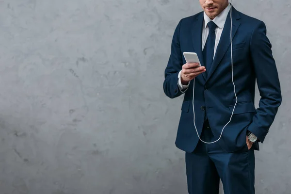 Recortado disparo de hombre de negocios escuchando música con auriculares y smartphone - foto de stock