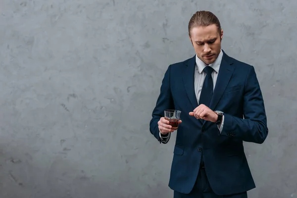 Young handsome businessman with glass of whiskey looking at watch — Stock Photo