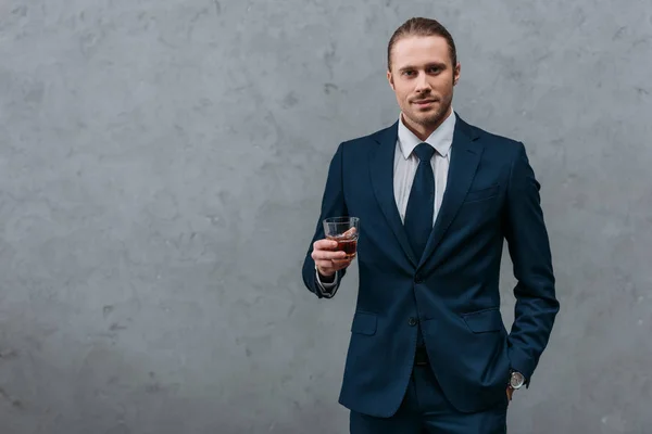Молодой уверенный бизнесмен со стаканом виски, смотрящий в камеру — стоковое фото