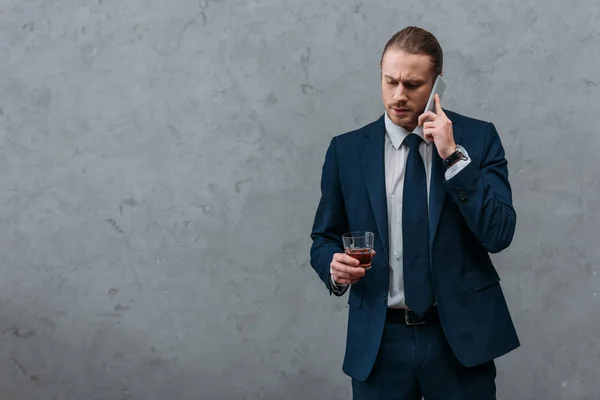 Jeune homme d'affaires sérieux avec un verre de whisky parlant par téléphone — Photo de stock