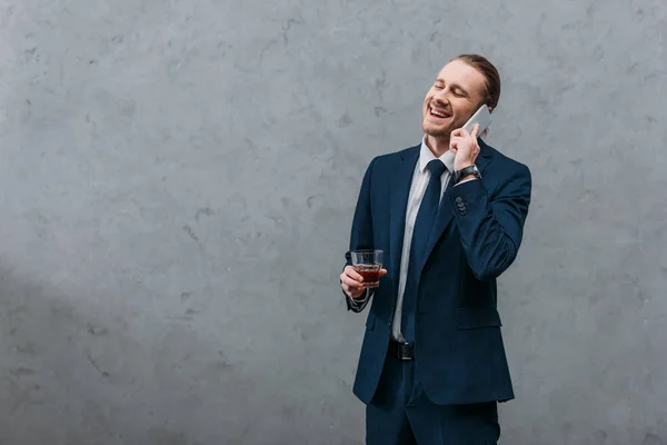 Giovane uomo d'affari ridente con bicchiere di whisky che parla per telefono — Foto stock