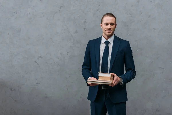 Junger gutaussehender Geschäftsmann hält Bücherstapel vor Betonwand — Stockfoto