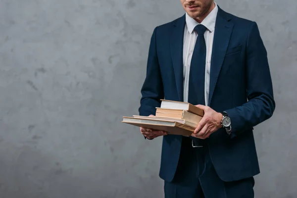 Cropped shot of businessman holding stack of books in front of concrete wall — Stock Photo