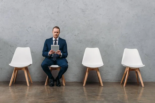 Молодой привлекательный бизнесмен, сидящий на стуле за планшетом — стоковое фото