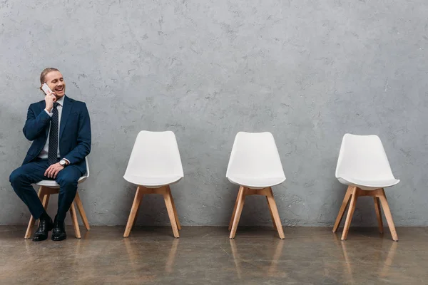 Young handsome businessman talking by phone while sitting on chair — Stock Photo