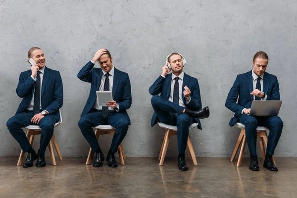 Коллаж клонированного молодого бизнесмена, сидящего на стульях и пользующегося гаджетами — стоковое фото