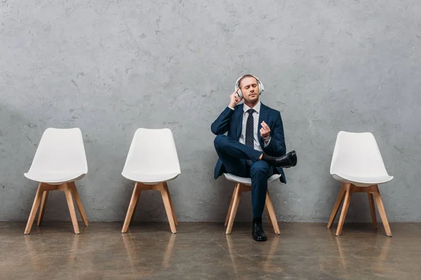 Young handsome businessman listening music with headphones while sitting on chair — Stock Photo