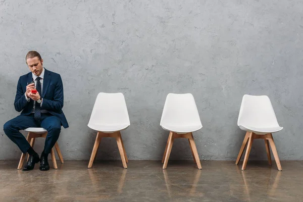 Lonely businessman sitting on chair and smoking in front of concrete wall — Stock Photo