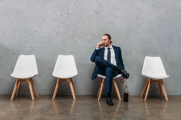 Empresario beber alcohol mientras está sentado en la silla debajo de la pared de hormigón - foto de stock