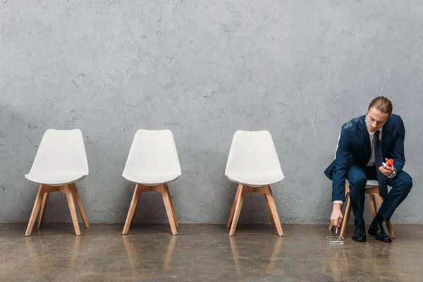 Самотній бізнесмен сидить на стільці і курить перед бетонною стіною — стокове фото