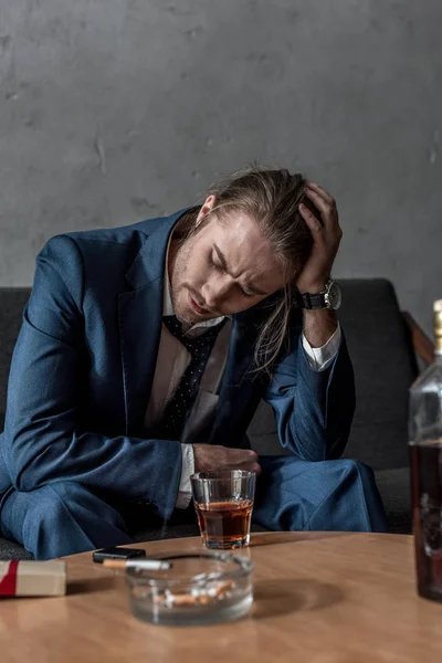 Пьяный бизнесмен, сидящий на диване со стаканом виски на столе — стоковое фото