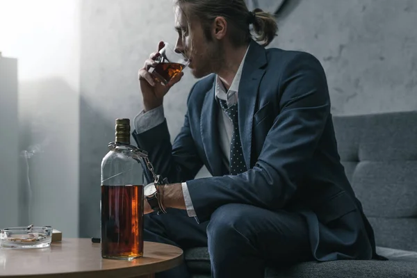 Homme d'affaires accro à l'alcool avec verre et bouteille de whisky assis sur le canapé — Photo de stock