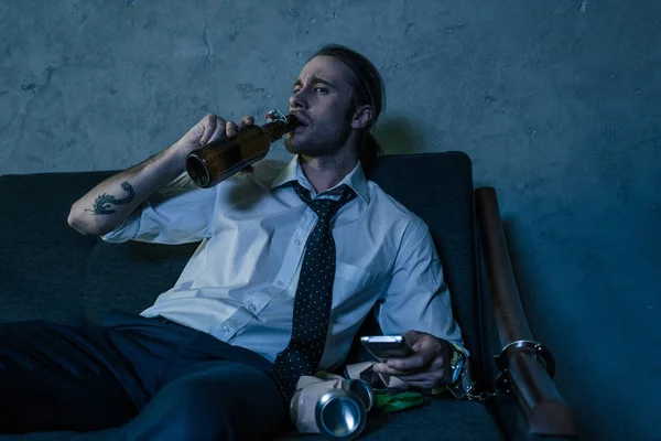 Young alcohol addicted man in white shirt watching tv and drinking beer after work — Stock Photo