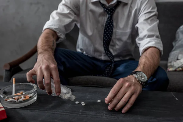 Homem de negócios com dependência de drogas derramando pílulas na mesa de garrafa — Fotografia de Stock