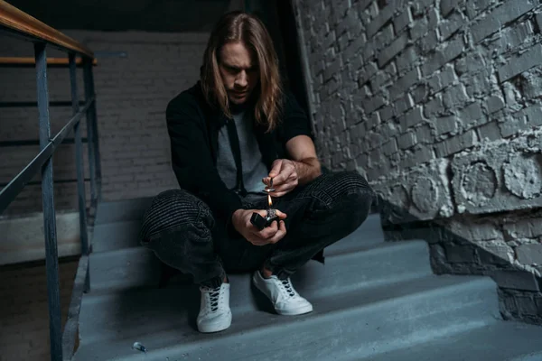 Addicted junkie boiling heroin in spoon with lighter on stairs — Stock Photo