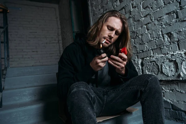 Young man smoking cigarette while sitting on stairs — Stock Photo