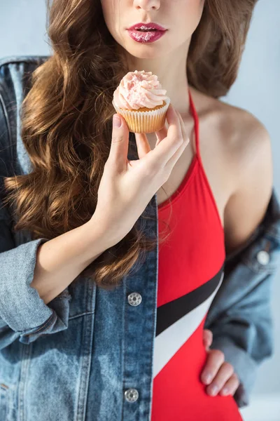 Cropped image of sexy girl in red swimsuit holding cupcake isolated on grey — Stock Photo
