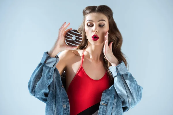 Chica sexy sorprendida en traje de baño rojo mirando donut aislado en gris - foto de stock
