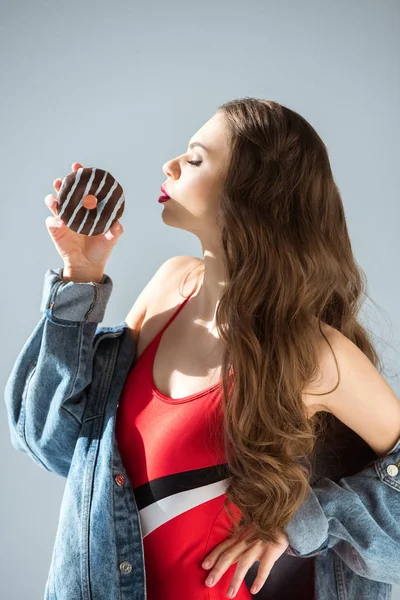 Seitenansicht von sexy Mädchen im roten Badeanzug küsst Donut isoliert auf grau — Stockfoto
