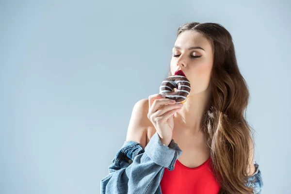 Sexy girl in red swimsuit biting donut with closed eyes isolated on grey — Stock Photo