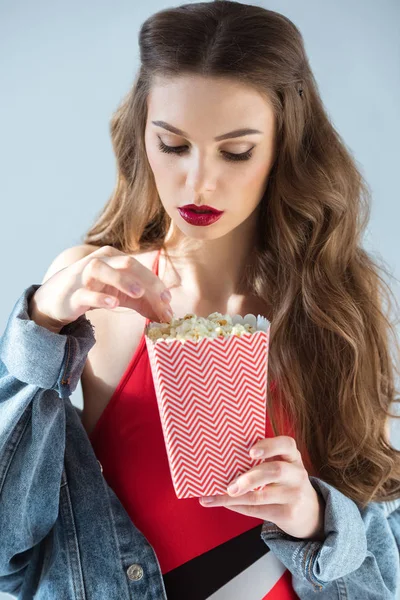 Sexy attraktives Mädchen mit roten Lippen nimmt Popcorn isoliert auf grau — Stockfoto