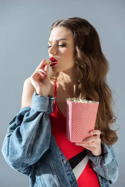 Atractiva chica sexy con labios rojos comer palomitas de maíz aislado en gris - foto de stock