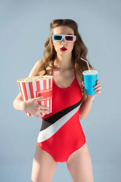 Seductive girl in 3d glasses holding popcorn with drink and looking at camera isolated on grey — Stock Photo