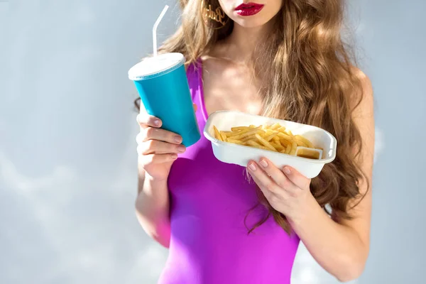 Imagen recortada de chica sexy en traje de baño ultra violeta con papas fritas en gris - foto de stock