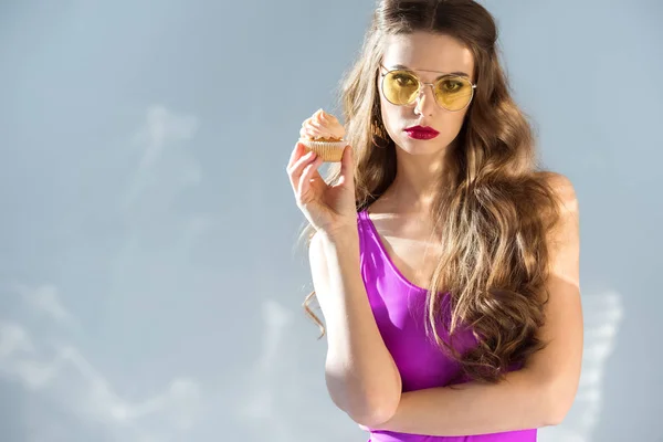 Sexy attractive girl in ultra violet swimsuit holding cupcake and looking at camera on grey — Stock Photo