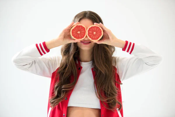 Sexy girl in baseball jacket covering eyes with grapefruit pieces isolated on white — Stock Photo