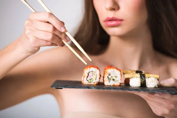 Imagem cortada de menina nua sexy tomando sushi com pauzinhos — Fotografia de Stock