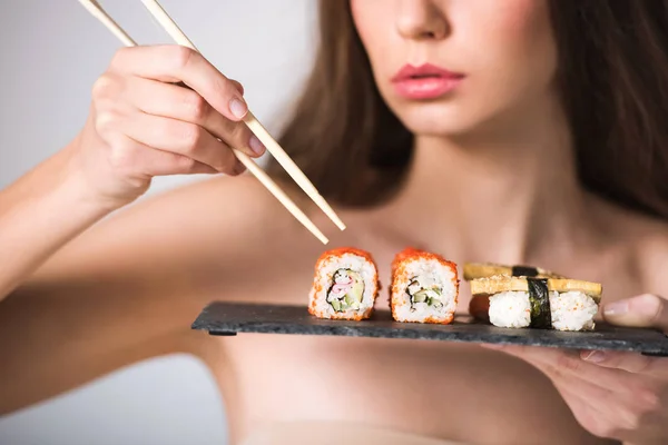 Imagen recortada de chica desnuda sexy tomando sushi con palillos - foto de stock