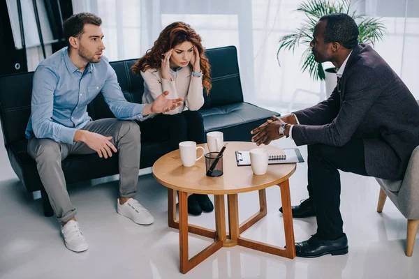 Frustrated young woman with boyfriend and african american counselor in office — Stock Photo