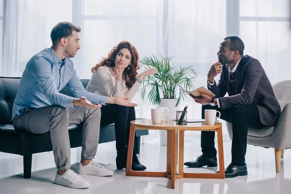 Quarreling couple talking to african american psychiatrist in office — Stock Photo