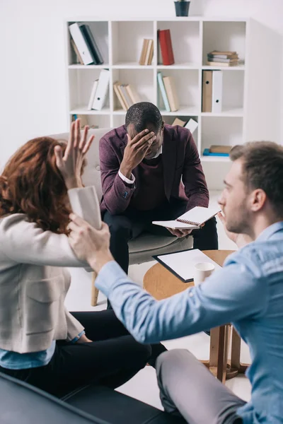 Frustrated african american psychiatrist with textbook and divorcing couple in office — Stock Photo