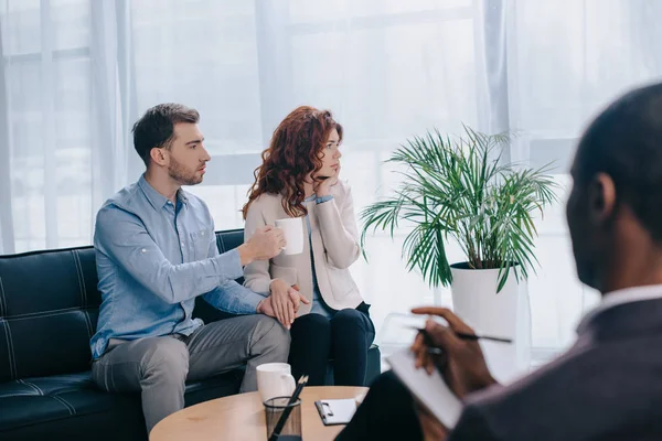 African american counselor with textbook and divorcing couple on sofa — Stock Photo